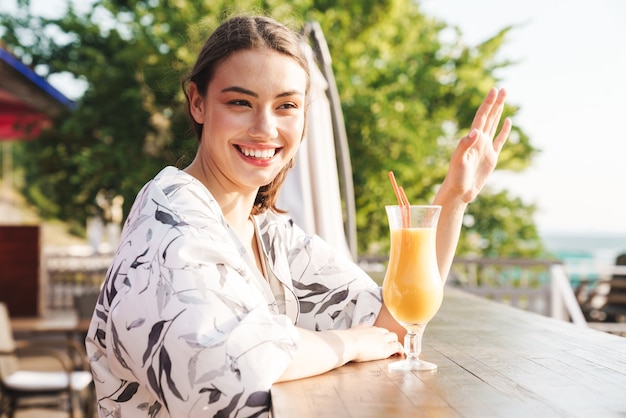 カフェでジュースカクテルを飲みながらビーチで元気で幸せな若い美しい女性を喜ばせます。