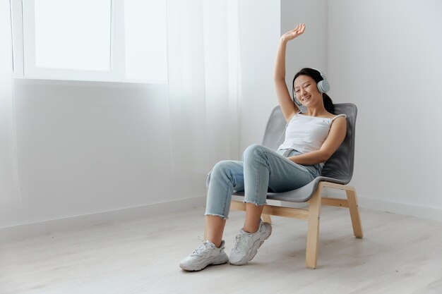 Cheerful happy relaxing tanned lovely young asian woman in\
headphones dance move to music at home interior living room sound\
studio stream social media concept cool offer banner wide\
angle