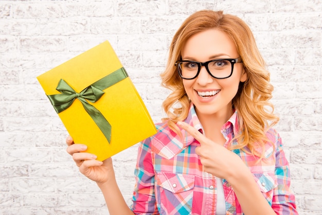 Cheerful happy woman in glasses pointing yellow box