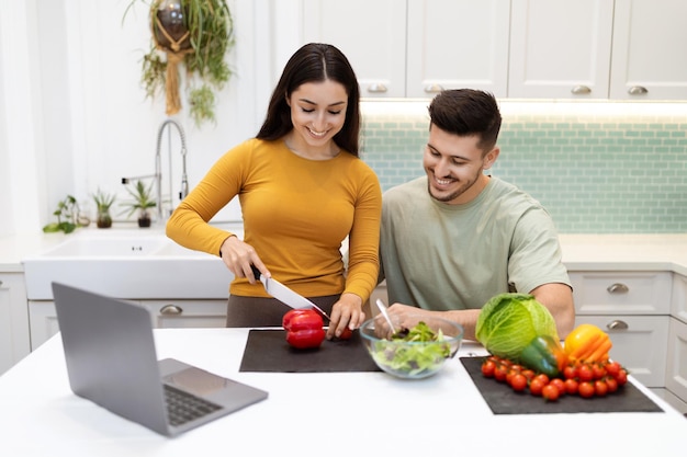 Cheerful hispanic couple looking for recipe on internet using laptop