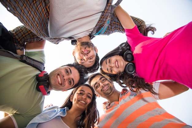 Cheerful Indian asian young group of college students forming a circle, looking downwords at camera