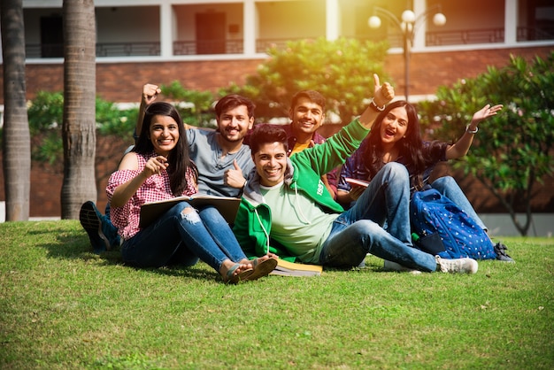 キャンパスで座ったり、立ったり、歩いたりしながら一緒に笑っている大学生や友人の陽気なインドのアジアの若いグループ