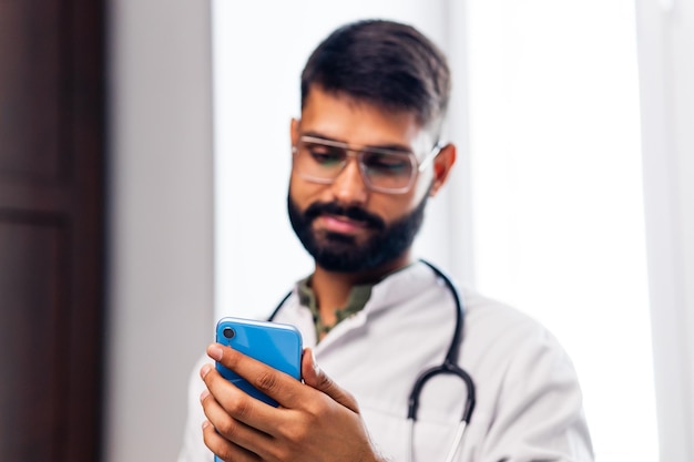 Cheerful indian doctor using application on mobile phone in hospital