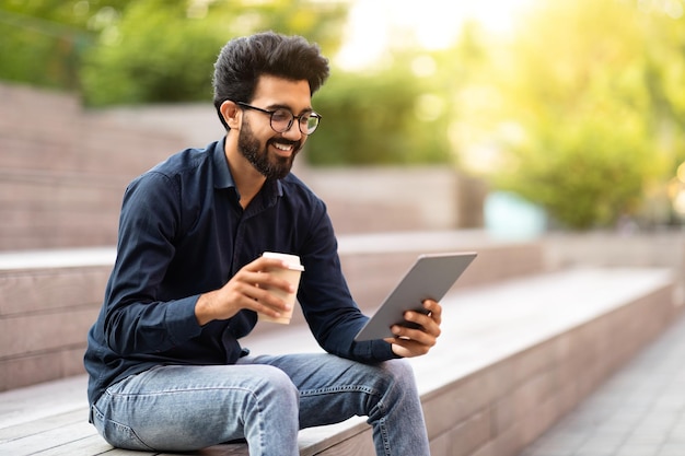 陽気なインド人男性がタブレットを屋外で使って一日働いた後に休んでいます