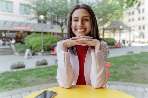 Cheerful Indian woman using laptop looking at camera having video conference job interview outdoors