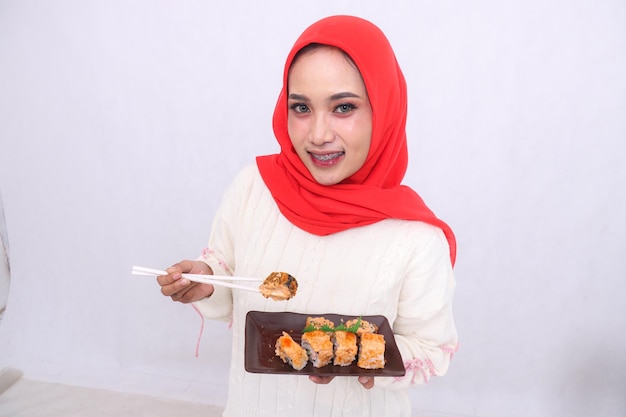 Cheerful indonesia woman in hijab top angle holds sushi chopsticks amp carries a plate containing su