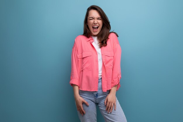 Cheerful joyful brunette lady in pink shirt and jeans on studio background