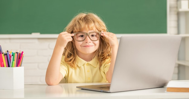 안경을 쓴 쾌활한 소년은 9월 노트북으로 학교 교실에서 온라인으로 공부합니다.
