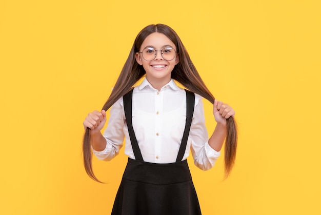 Foto il bambino allegro tiene i capelli lunghi in uniforme scolastica e gli occhiali per proteggere i capelli dalla vista