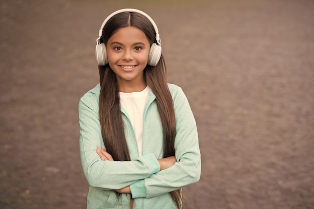 Cheerful kid wear earphones with music song outdoor enjoying melody elearning education