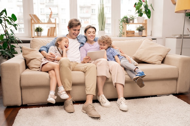 Photo cheerful kids and their parents in casualwear relaxing on couch in living-room