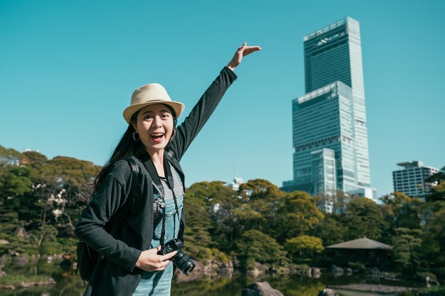 cheerful lady photographer taking picture with highest skyscraper in abeno ku area in osaka city. happy girl showing how high the modern building of hotel. smiling woman tourist face camera joyful.