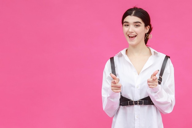 Cheerful lady pointing her fingers to the camera and standing on pink background