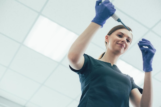 Cheerful lady in rubber gloves holding a dropping tube and smiling