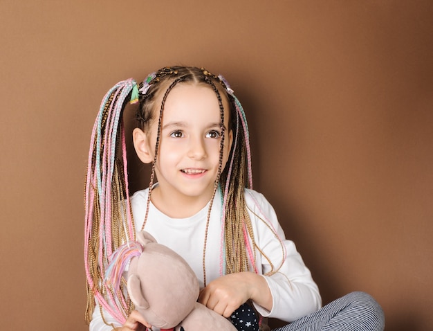 Photo cheerful laughing girl 5 years old with multicolored pigtails in a white tshirt on a brown surface