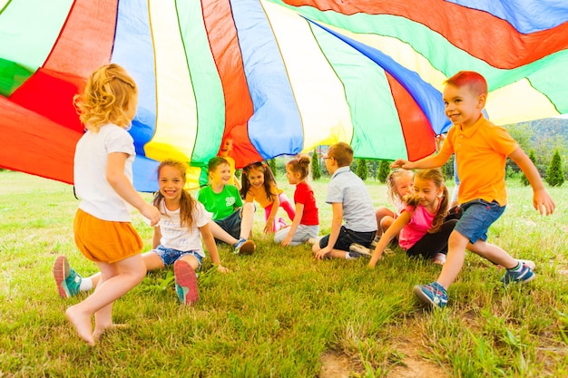 Cheerful and laughing kids hiding under large rainbow canopy, summer outdoors activities concept