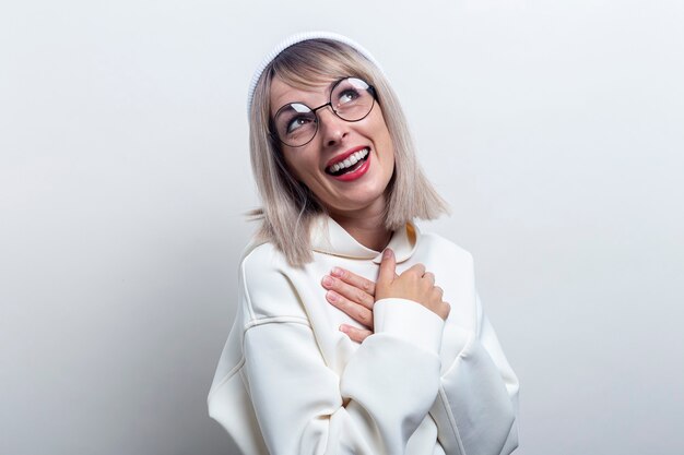 Cheerful laughing young woman in glasses in a hoodie on a light background.