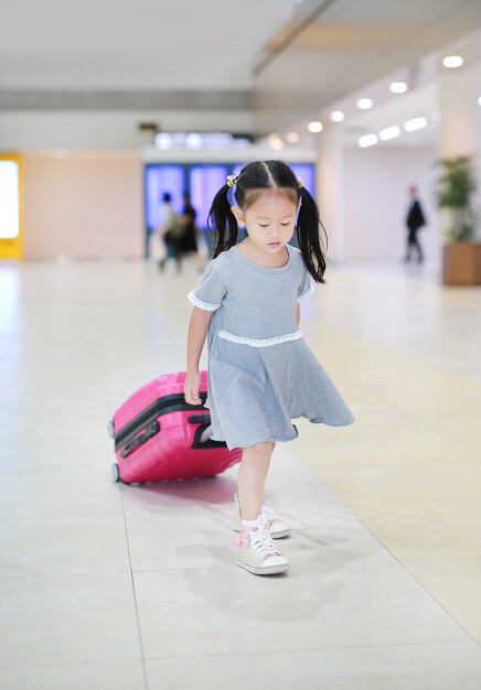 Cheerful little asian girl walking with luggage at the airport