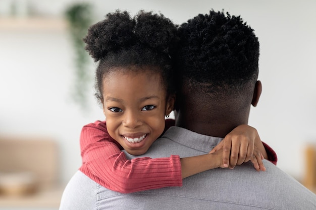 Cheerful little black girl hugging her daddy