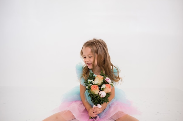 A cheerful little blonde girl sits with a bouquet of flowers on a white background with a place for text