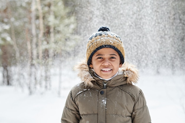 Cheerful little boy of african ethnicity wearing warm winter jacket and beanie