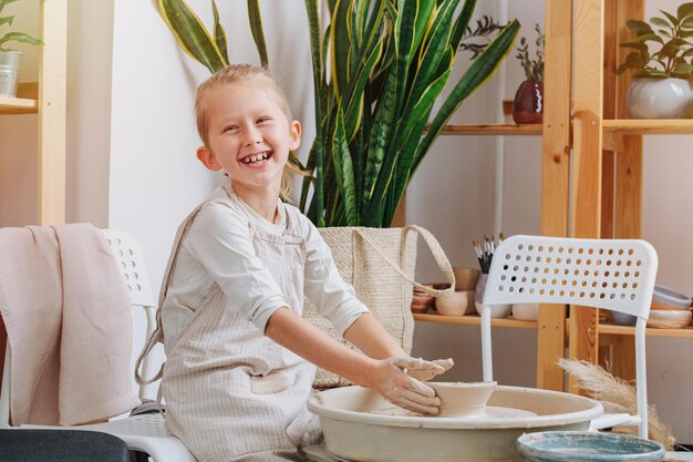 Cheerful little boy shaping clay vase on a pottery wheel in a workshop