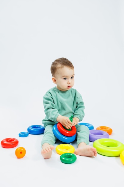 Cheerful little boy sitting with plastic educational toys on a white background Child and toys for development Development of children's motor skills