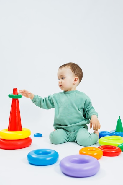 Cheerful little boy sitting with plastic educational toys on a white background Child and toys for development Development of children's motor skills