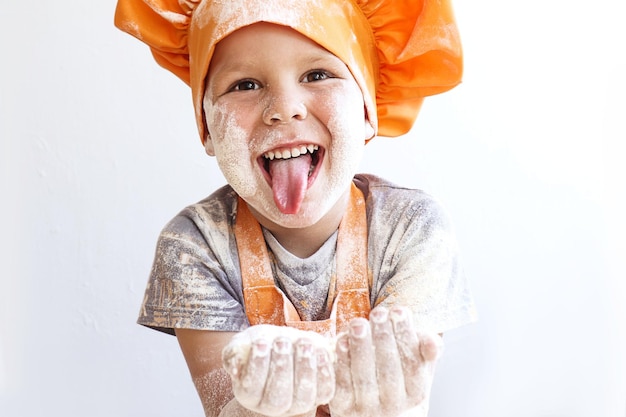 Cheerful little cook with flour in his hands shows his tongue closeup