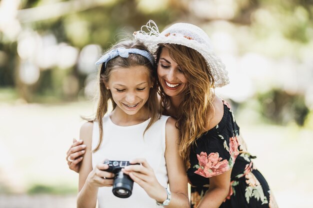 写真 陽気な少女と彼女の若いお母さんは、デジタルカメラで写真を見て、公園で夏休みを楽しんでいます。