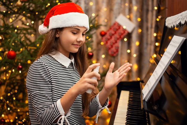 Cheerful little girl applying hand sanitizer before playing the piano after another person to protect herself from Covid