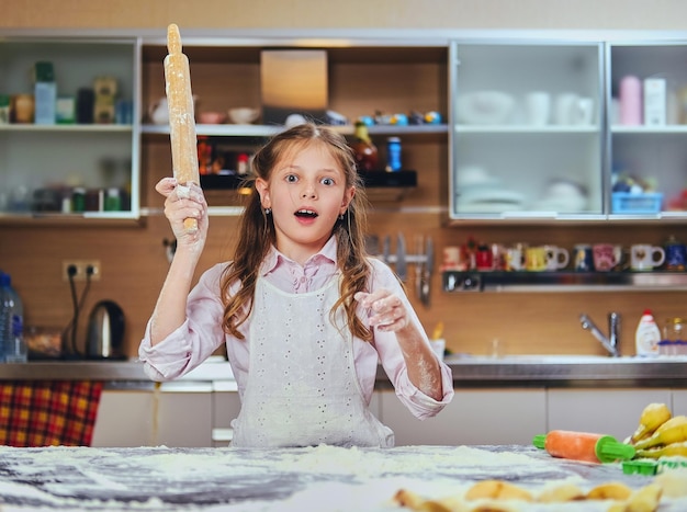 Cheerful little girl cooking dough at the kitchen.