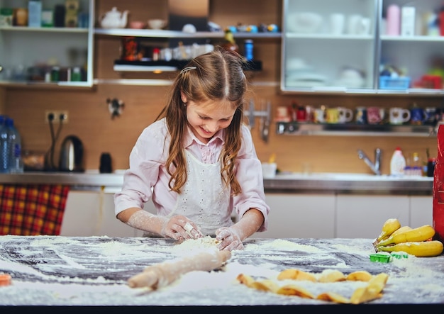 Cheerful little girl cooking dough at the kitchen.