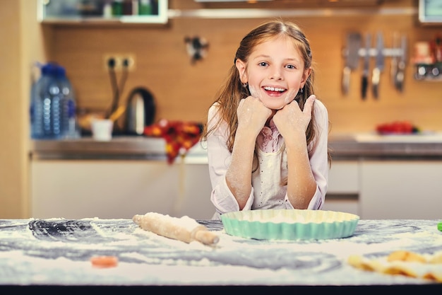 Cheerful little girl cooking dough at the kitchen.