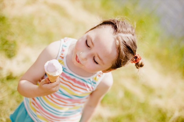 Cheerful little girl eating ice cream in the summer in the park