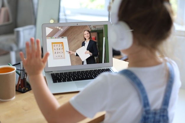 Веселая маленькая девочка девочка в наушниках с помощью ноутбука учится через систему электронного обучения онлайн