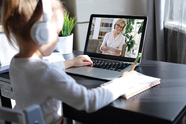 Cheerful little girl girl in headphones using laptop studying through online elearning system