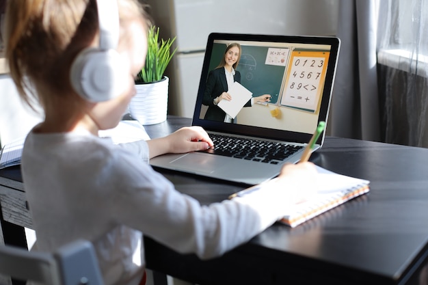 Cheerful little girl girl in headphones using laptop studying through online elearning system