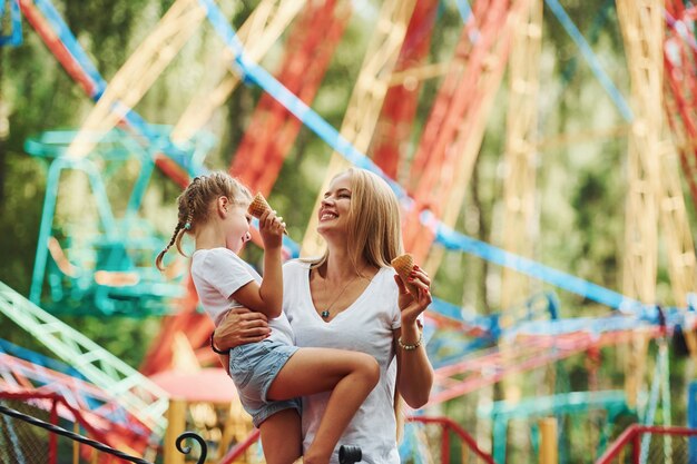 Photo cheerful little girl her mother have a good time in the park together near attractions