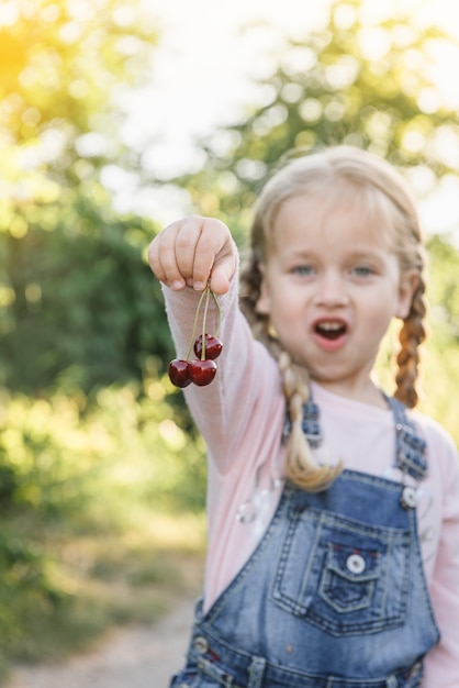 Cheerful little girl holding cherries in the garden in summer