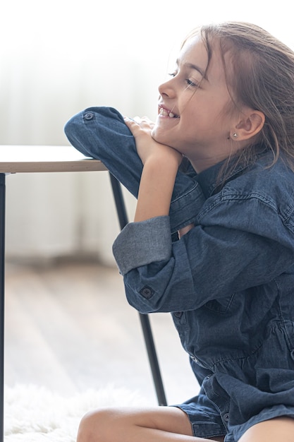 Cheerful little girl is sitting at a table on a cozy rug in her room at home.