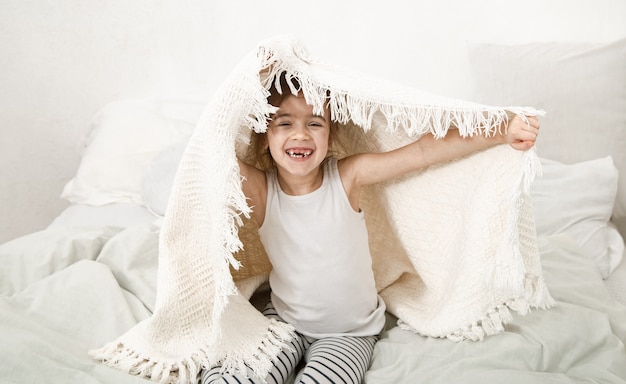 Cheerful little girl plays with a blanket after sleep. Baby sleep and rest concept close up.