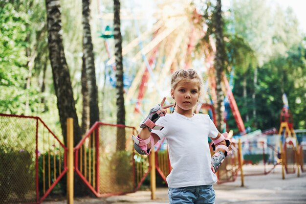 La bambina allegra sui pattini a rotelle si diverte nel parco vicino alle attrazioni