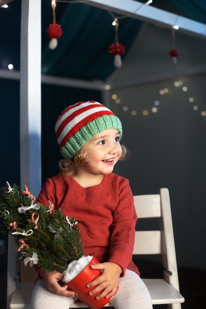 Cheerful little girl santa hat holding small christmas tree hands