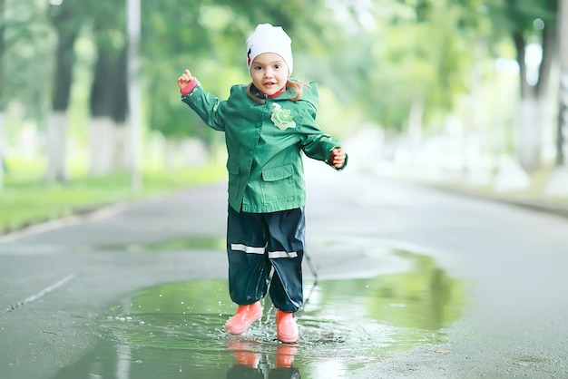 веселая маленькая девочка ходит и прыгает в лужи под дождем