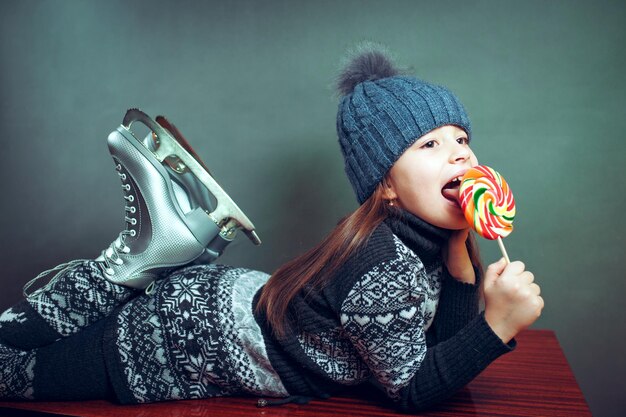 Cheerful little girl in warm sweater and hat holding figure skates.