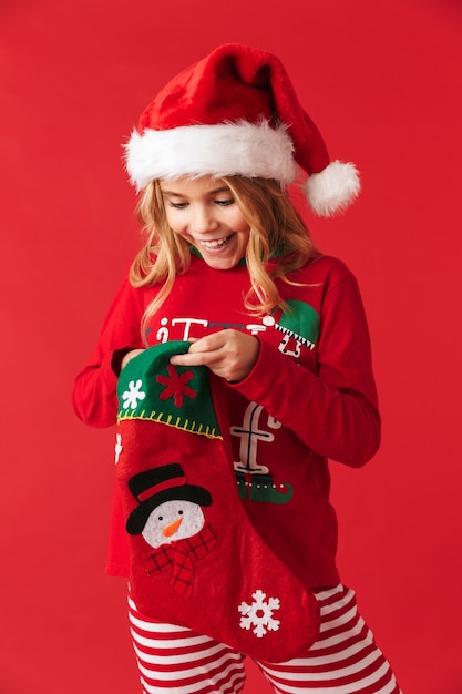 Веселая маленькая девочка в рождественском костюме стоит изолированно, принимая подарки из рождественского носка