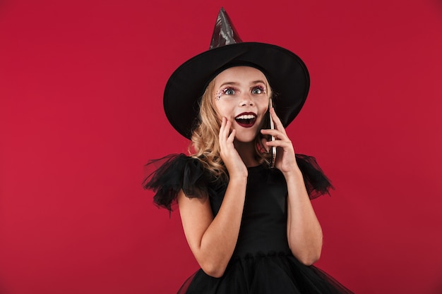 Cheerful little girl wearing Halloween witch costume standing