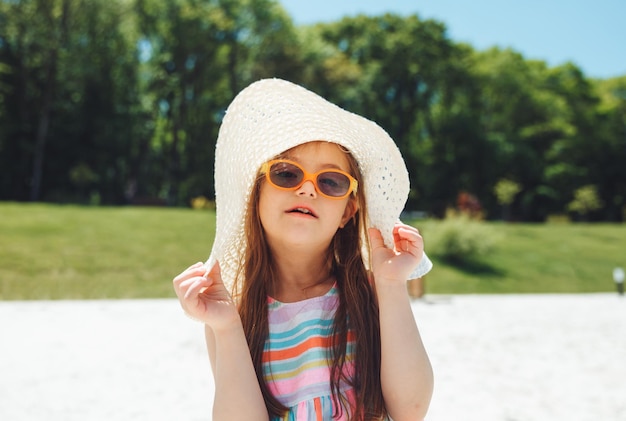 Cheerful little girl with down syndrome in a summer hat on the beach