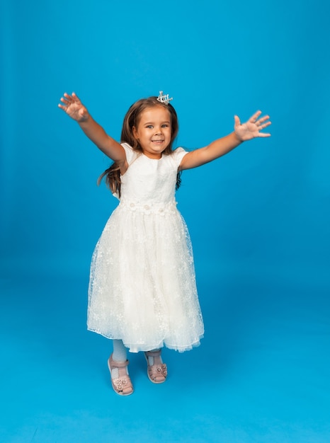 Cheerful little girl with long hair in a princess dress and with a crown.